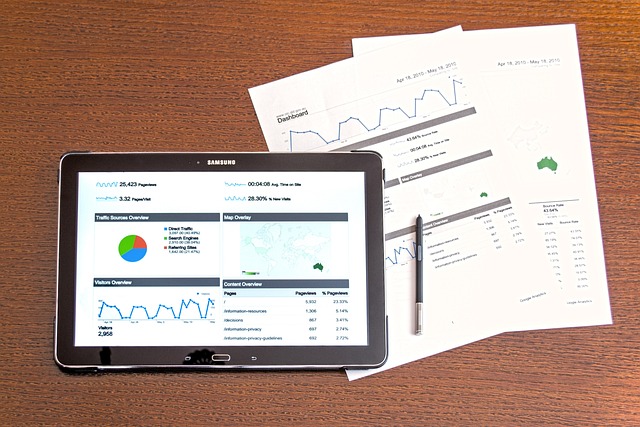 Tablet och papper med analystrapporter på trämöbel.