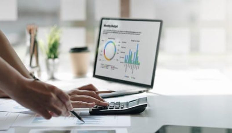 Kontorsarbete med laptop och grafer på skärm, händer skriver och räknar.